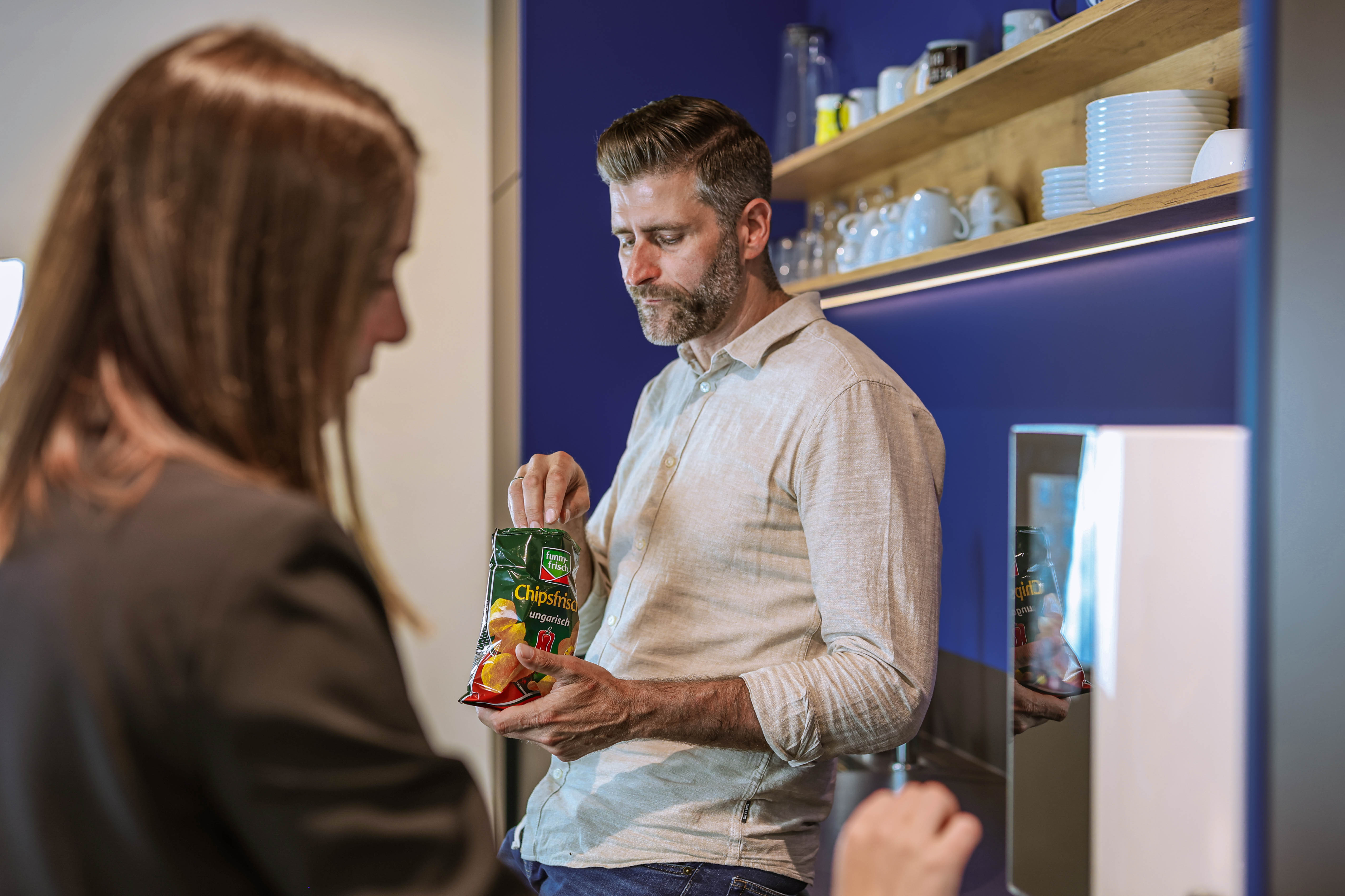 Mitarbeiter nimmt Chips aus Snackpackung in Büro-Küche